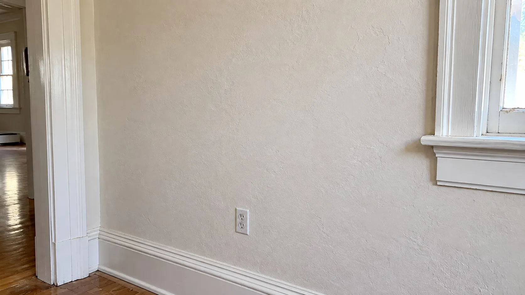 Repaired plaster wall in an older home, smooth and painted between the original door casing and window trim
